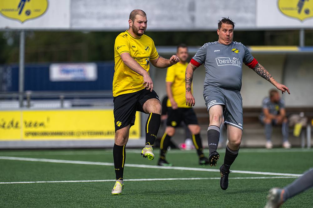 Duel om de bal tussen een speler in het geel en een speler in het grijs.