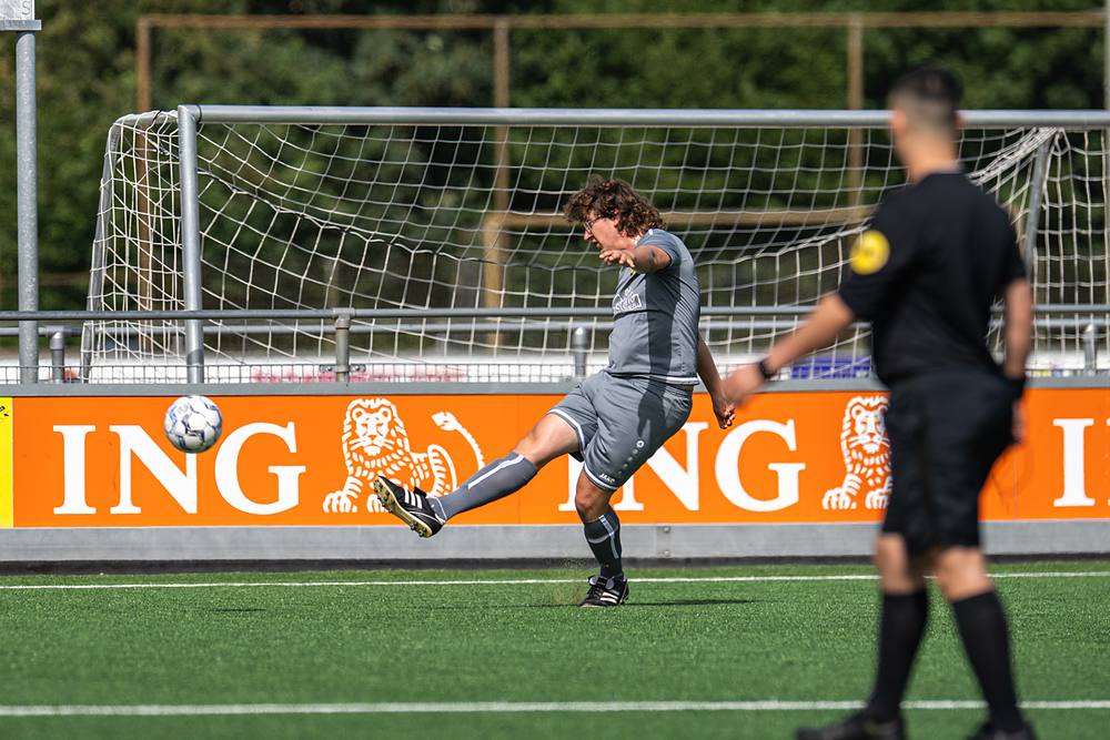 Speler in het grijs haalt uit voor doel, de scheidsrechter kijkt toe.