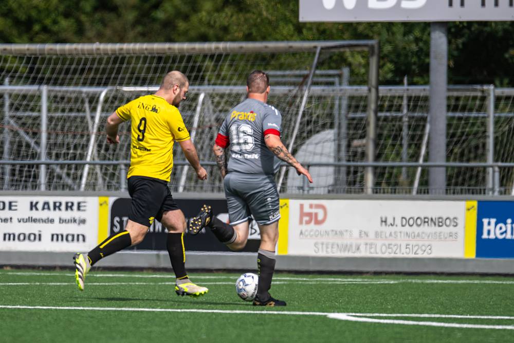 Sprintduel tussen een aanvaller in het geel en een verdediger in het grijs.
