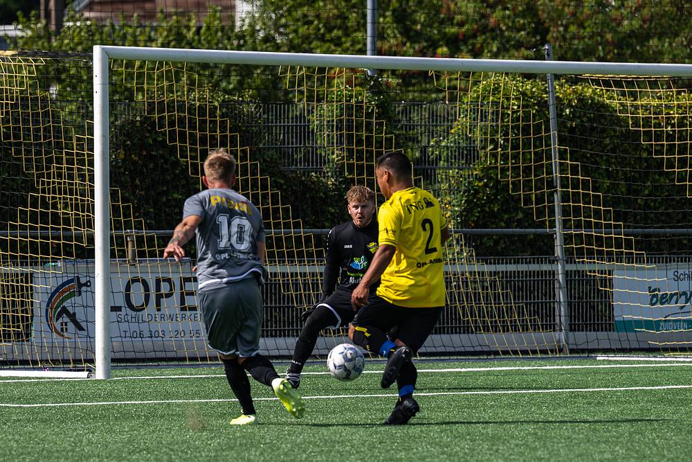 Doelmondactie: spelers in geel en grijs duiken op de bal voor het doel.