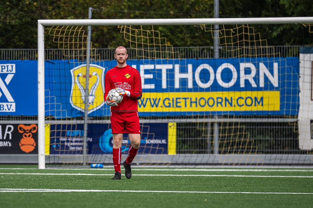 De keeper in het rood pakt de bal op voor het doel.