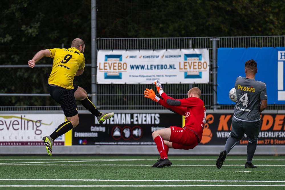 Speler in het geel haalt uit terwijl de keeper zich lang maakt.